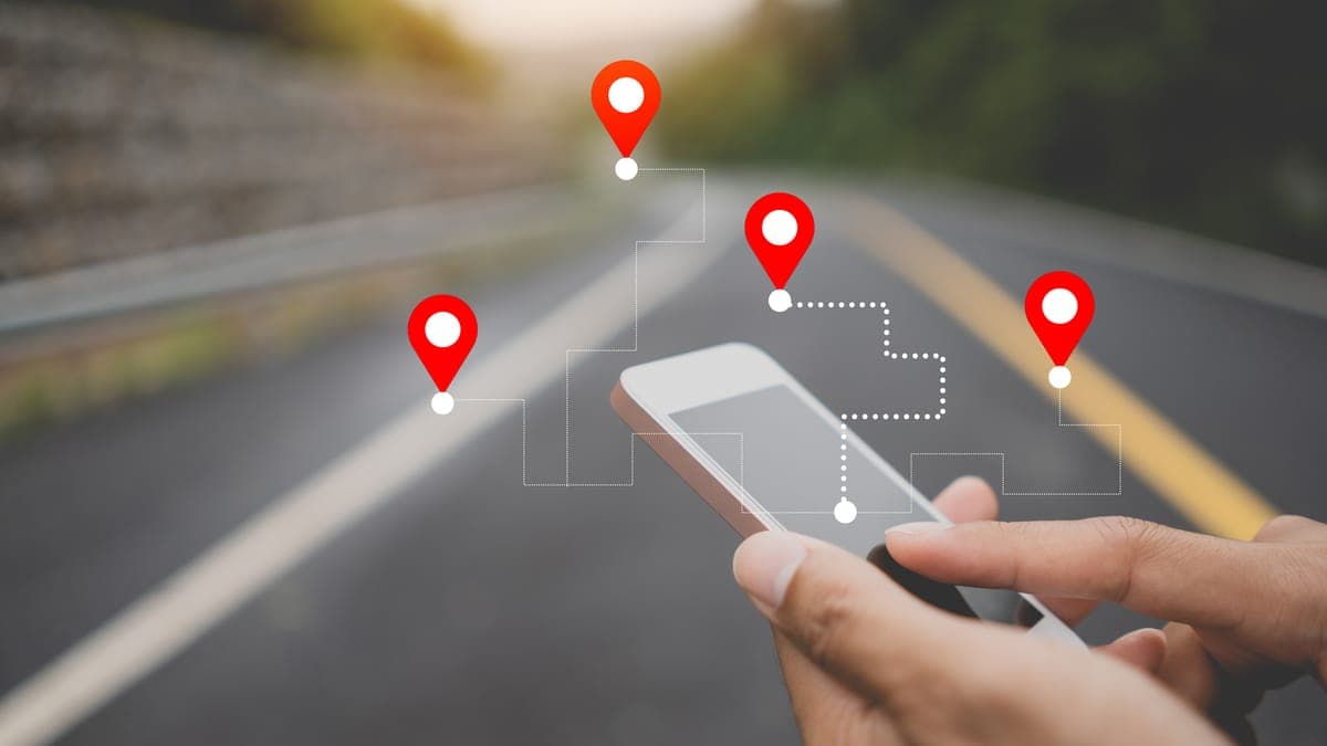 Hands holding a smartphone on a road with red map location pins above it