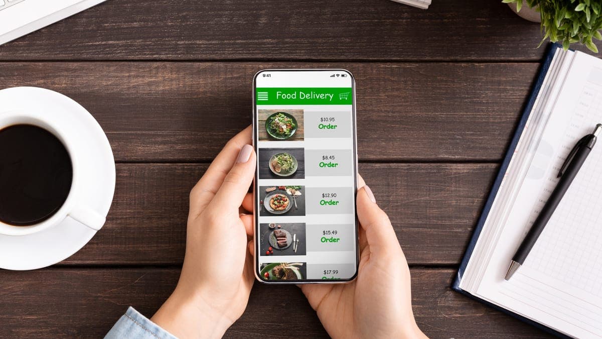 Hands scrolling a food menu with prices on a smartphone above a wooden desk