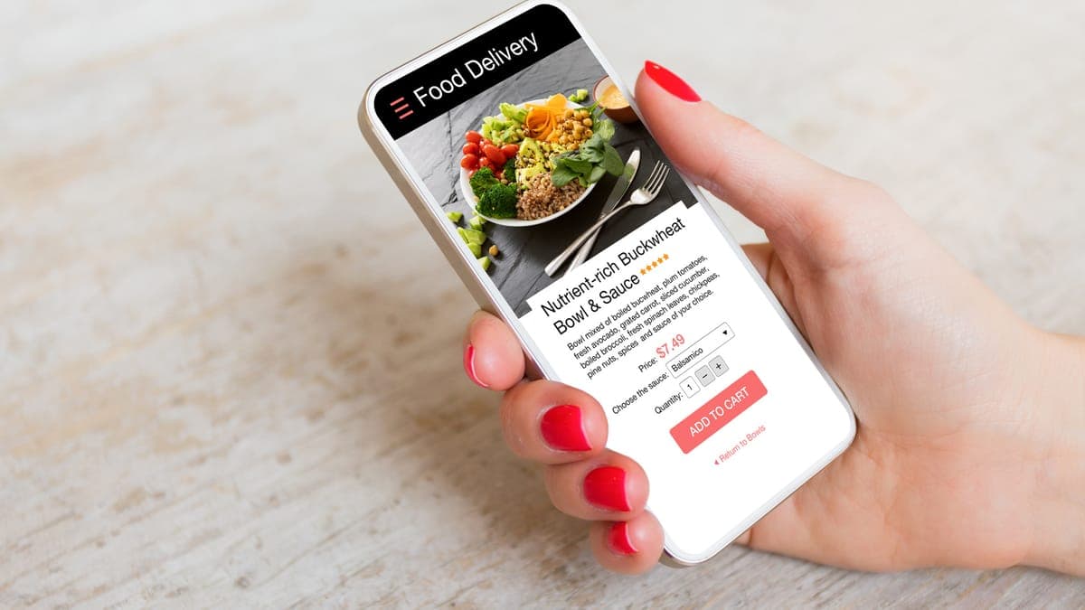 Hand holding a smartphone showing a food ordering page with an add to cart button