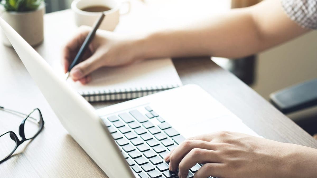 Man taking notes from his laptop while writing