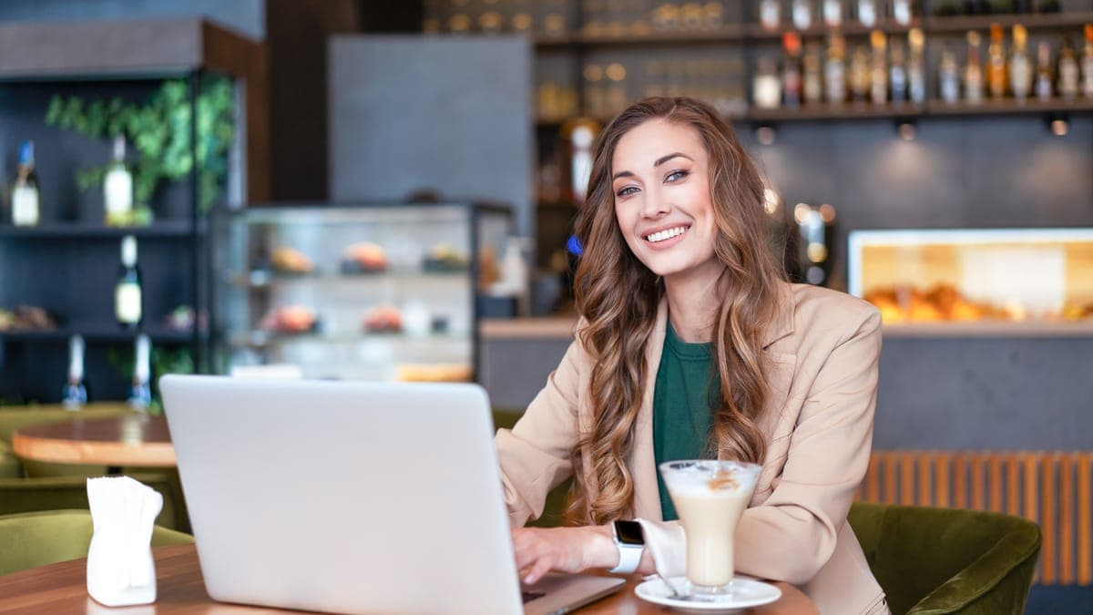 Smiling woman working on a laptop at a table in a restaurant with a bar behind