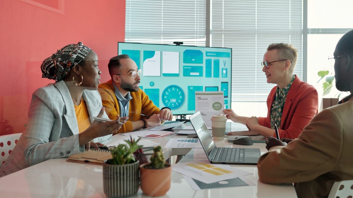 Agency team talking around a meeting table with laptops and a large screen