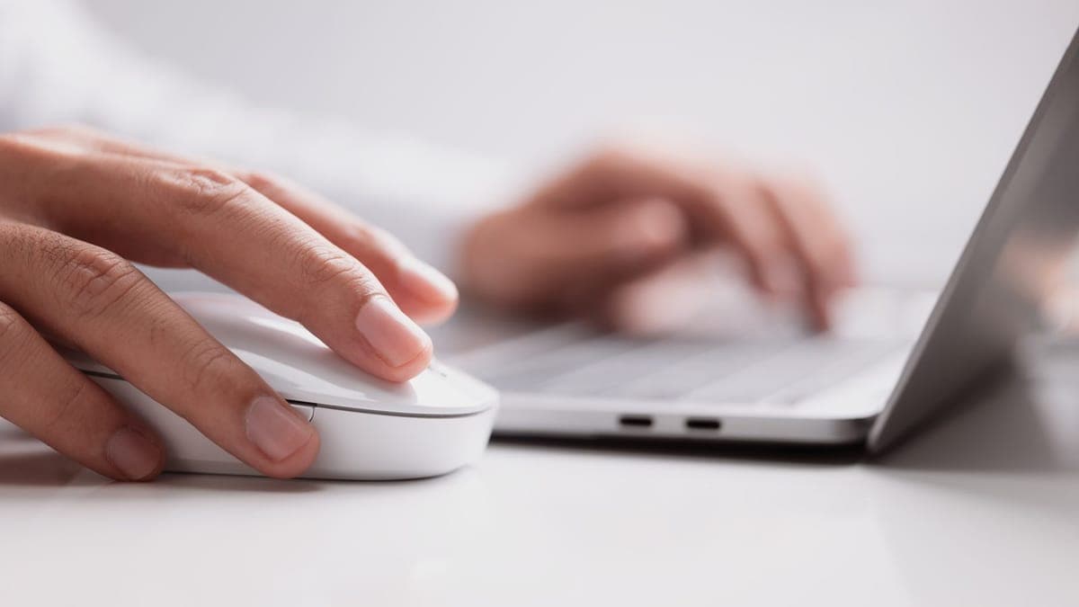 Hand on a computer mouse next to a laptop keyboard