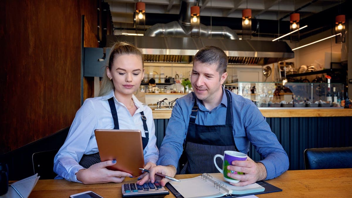 Two restaurant owners in aprons going over accounts with a calculator and tablet